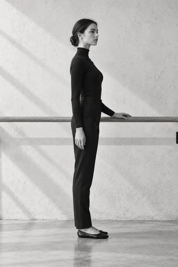 A woman standing tall beside a ballet barre in side view