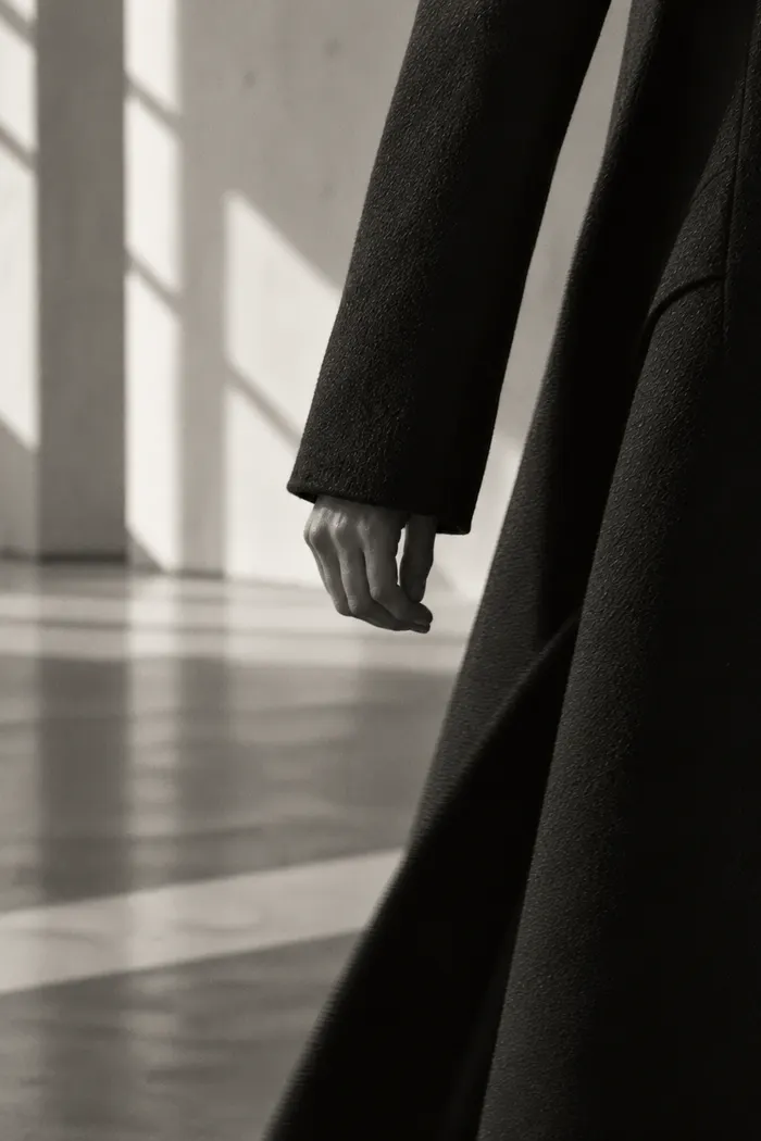 Close-up of a relaxed hand at the side of a long black coat