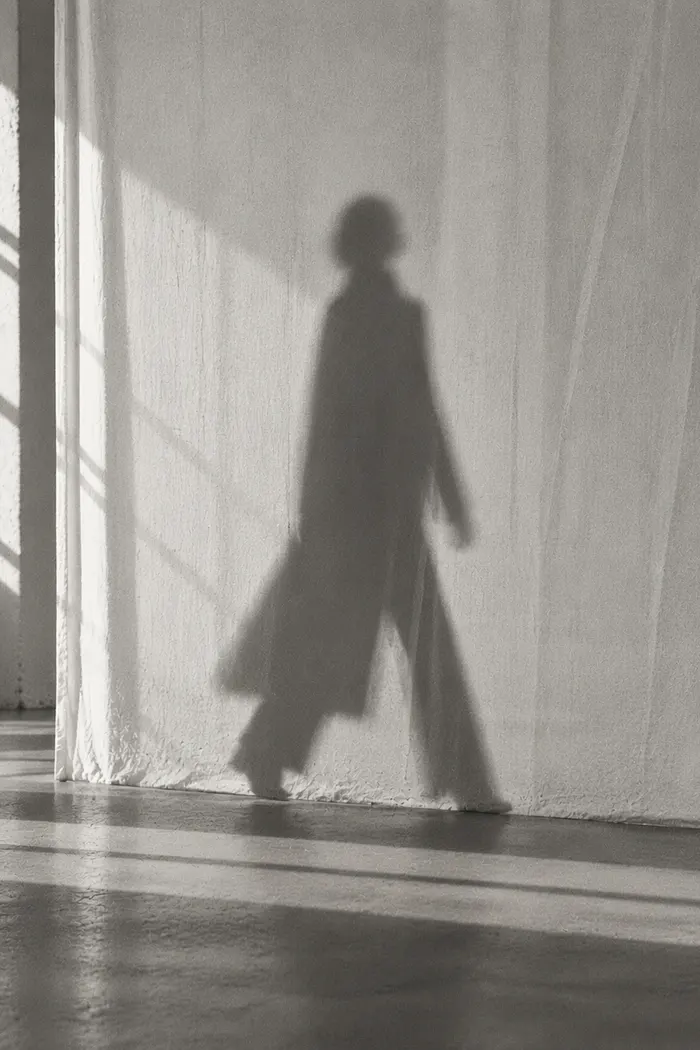 An editorial shadow of a walking figure on a white curtain