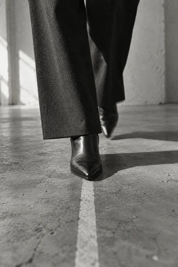 Pointed black boots stepping along a painted line on a concrete floor