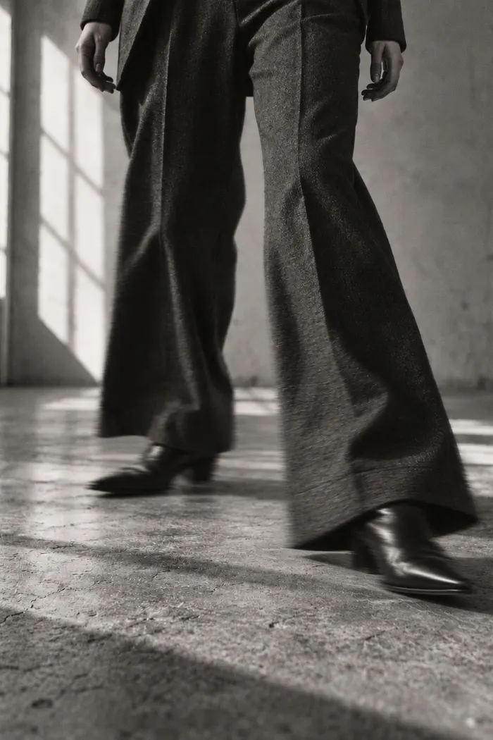 Wide trousers and pointed boots mid-stride, front heel landing just ahead of the body
